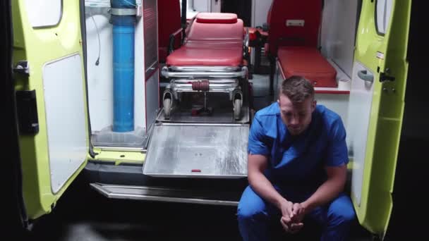 Грустный санитар сидит в машине скорой помощи ночью . — стоковое видео