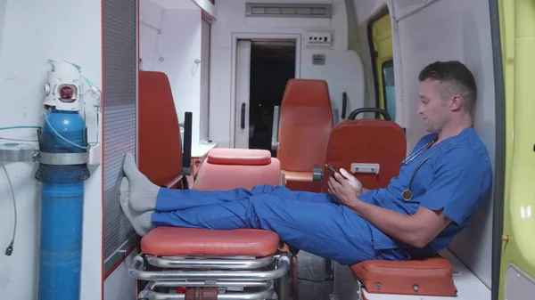 Hombre sentarse con el teléfono en coche ambulancia, ver algo y sonreír . — Foto de Stock