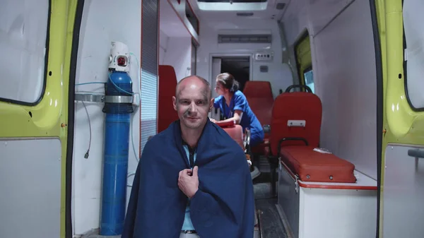 Hombre enfermo en manta sentarse y sonreír, en la enfermera de fondo . — Foto de Stock