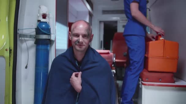 Homme en couverture assis dans une ambulance voiture en couverture et sourire . — Video