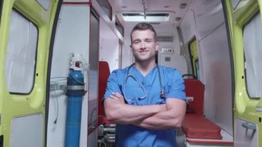 Ambulans vagonunun arka planında tıbbi üniformalı adam duruyor..