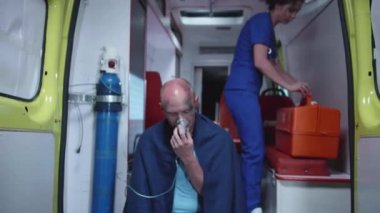 Hasta adam ambulans vagonunda oksijen maskesi içinde oturmuş.