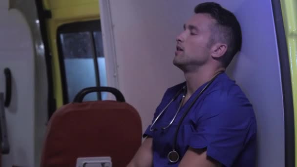 Уставший санитар сидит в машине скорой помощи . — стоковое видео