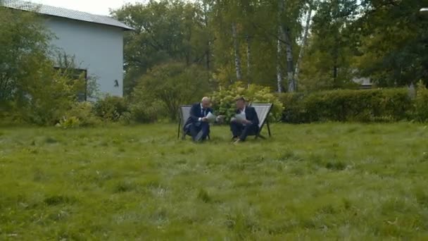 Men in suits sit in courtyard with papers and chat. — Stockvideo