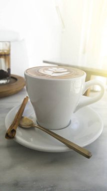 Yakın çekim latte, Cappuccino Kahve Kupası beyaz ve köpüklü köpük tarçın sopayla yan çanak beyaz masaya koy..