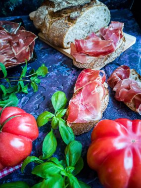 Jambon, domates, ekmek ve kompozisyon kaba tekstürlü koyu arka plan üzerinde otlar