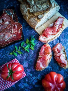 Jambon, domates, ekmek ve kompozisyon kaba tekstürlü koyu arka plan üzerinde otlar