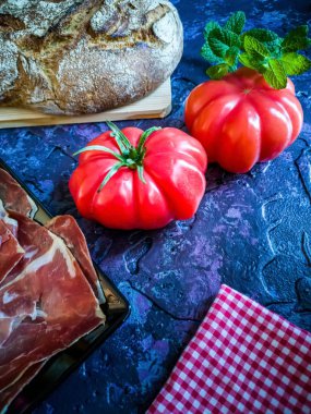 Jambon, domates, ekmek ve kompozisyon kaba tekstürlü koyu arka plan üzerinde otlar