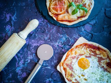 Koyu arka planda ev yapımı pizzalar ve çatal bıçaklar, leylak tonlarında.