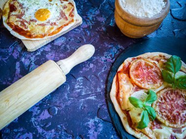 Koyu arka planda ev yapımı pizzalar ve çatal bıçaklar, leylak tonlarında.