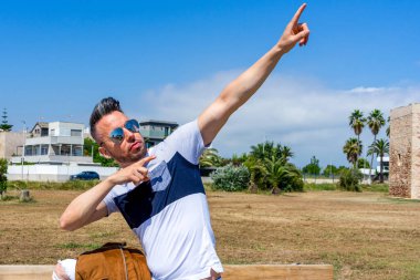 Beyaz giyinmiş genç bir adam ve modern bir stil. Tahta bir bankta oturuyor. Moda konsepti