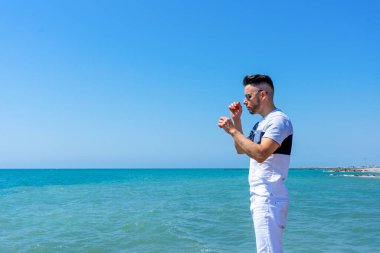 Beyaz pantolonlu genç adam ve modern stil Burriana 'daki Akdeniz sahilinde poz veriyor. Moda konsepti