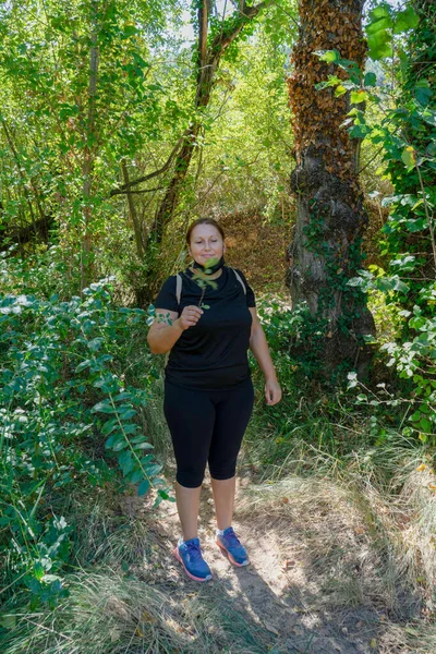 Ormanda elinde bir bitkiyle siyah giyinmiş orta yaşlı bir kadın. Doğa konsepti