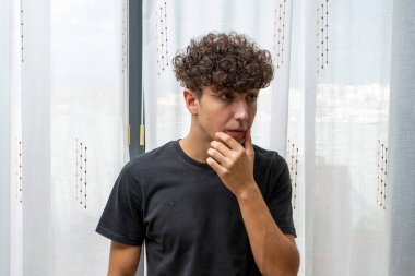 Beyaz perde arkasında siyah tişört giyen kıvırcık saçlı çekici genç adam. Moda konsepti