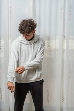 Beyaz perde arkasında poz veren kıvırcık saçlı, beyaz kazaklı çekici bir genç. Moda konsepti