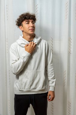 Beyaz perde arkasında poz veren kıvırcık saçlı, beyaz kazaklı çekici bir genç. Moda konsepti