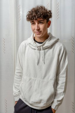 Beyaz perde arkasında poz veren kıvırcık saçlı, beyaz kazaklı çekici bir genç. Moda konsepti