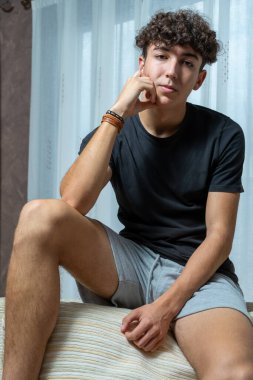 Beyaz perde arkasında siyah tişört giyen kıvırcık saçlı çekici genç adam. Moda konsepti