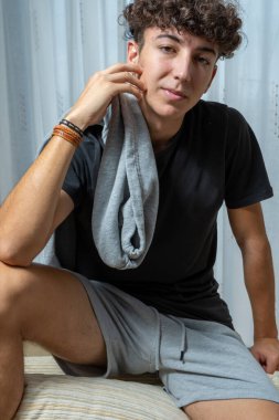 Beyaz perde arkasında siyah tişört giyen kıvırcık saçlı çekici genç adam. Moda konsepti