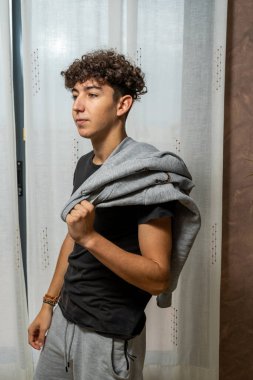 Beyaz perde arkasında siyah tişört giyen kıvırcık saçlı çekici genç adam. Moda konsepti