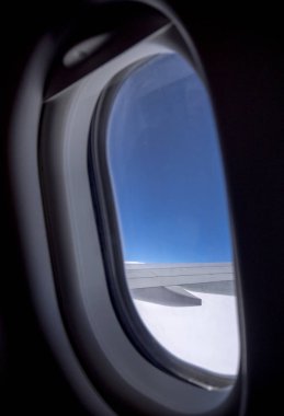 Uçuş sırasında mavi gökyüzü ile pencereden uçak kanadı bakıyor.