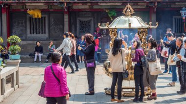 Taipei, Tayvan - 13 Mart 2019: Tayvan'ın en ünlü tapınağı Longshan tapınağında altın dev tütsü brülörü ile dua eden ve tütsü sunan insan kalabalığı.
