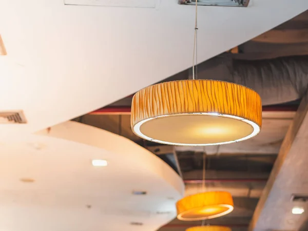 Round and flat modern hanging lamp in food court with yellow sunlight through windows.