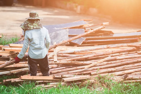 A woman construction laborer carrying wood beam on green grass.