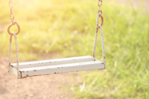 Empty old rusted metal swing in playground at the morning with yellow sunlight. Loneliness concept.