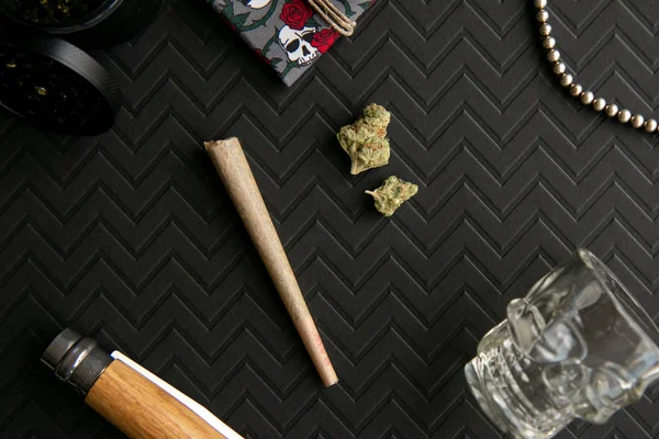 Marijuana joint and buds against a chevron black background with accessories
