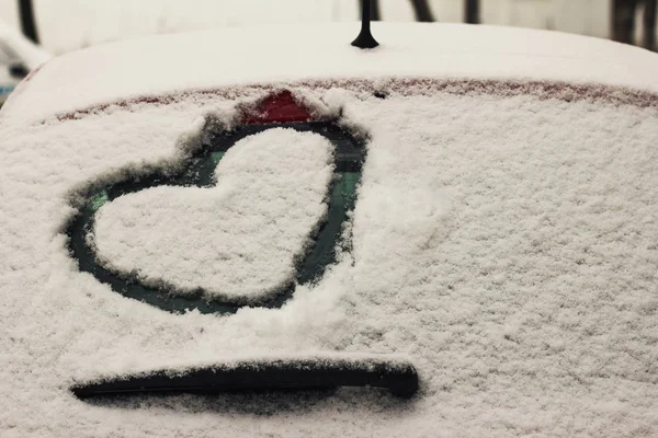 Heart drawn on a car windshield covered with fresh snow