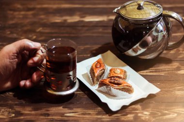 Siyah çay Azeri baklava ve çaydanlık üzerinde ahşap masa üzerinde yakınındaki bir bardak tutan el arka plan