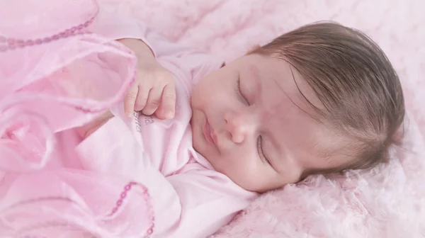 Baby girl asleep on pink bed. Newborn. Pink clothes.