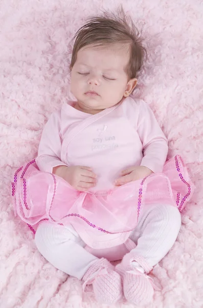 Baby girl asleep on pink bed. Newborn. Pink clothes.