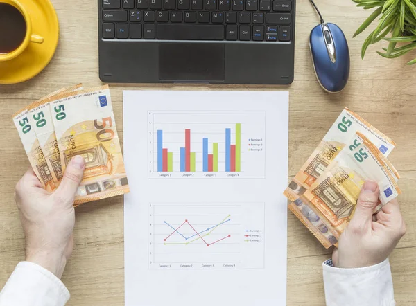 Man's hands with money on desktop. Office desktop on wooden background. Accounts balance. Top view. Euro.