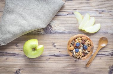 Ahşap zemin üzerinde müsli, badem, yaban mersini, ceviz ve elma ile sağlıklı kahvaltı. Üstte görüntü.