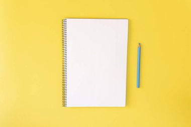 Sarı arka planda boş defter ve mavi kalem, üst manzara. Boşluğu kopyala.