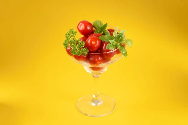 Cherry tomatoes in a cocktail glass on the yellow background.
