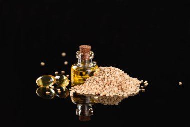 Cam şişede susam yağı ve siyah arka planda susam tohumu..