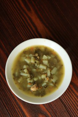 Tahta bir masanın üzerinde beyaz bir tabakta kuş çorbası.