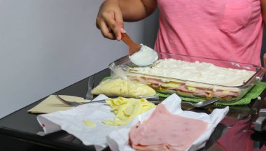 Kadınların elleri lazanya, makarna, jambon ve peynir pişiriyor.