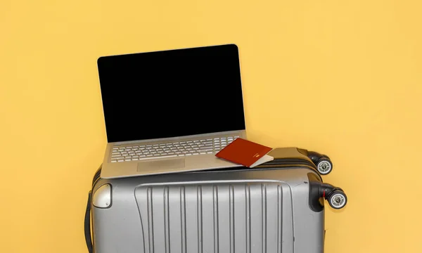 a laptop, and passport on a silver travel suitcase, internet and travel concept, yellow background