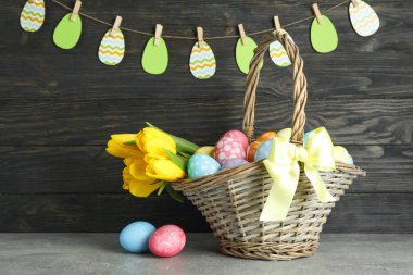 Renkli yumurta ve çiçek ahşap arka plan üzerinde Paskalya sepeti dolu
