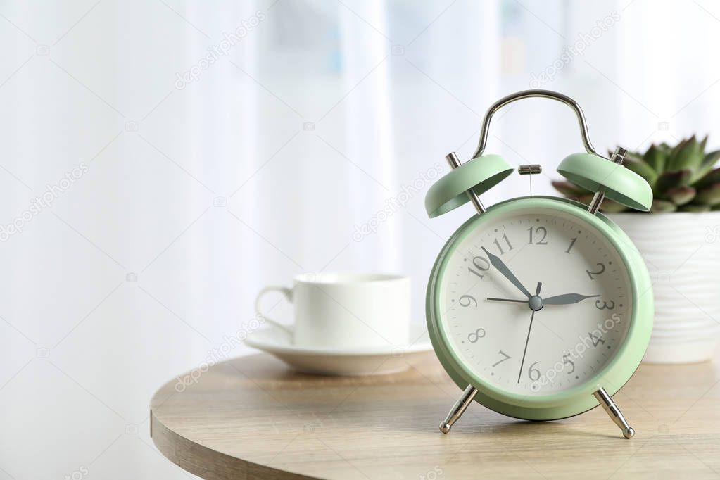 Beautiful retro alarm clock with cup of coffee and succulent pla