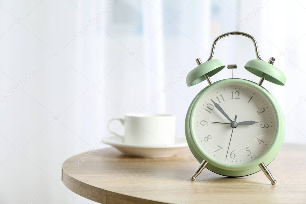 Beautiful retro alarm clock with cup of coffee on table against 