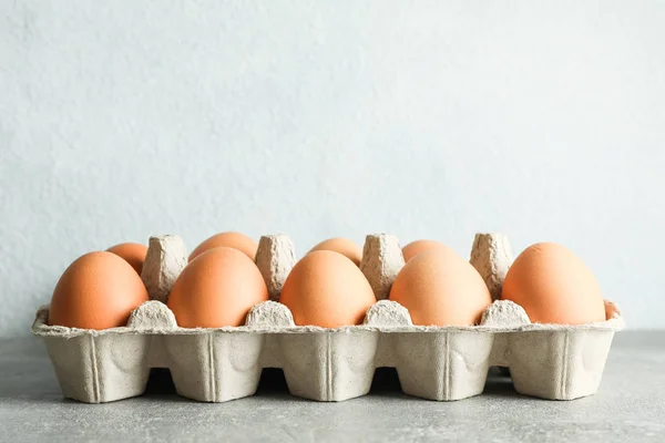 Chicken eggs in carton box on gray background, space for text