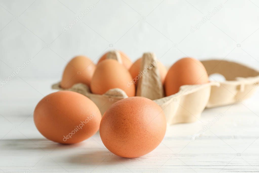 Chicken eggs in carton box on wooden table against white backgro