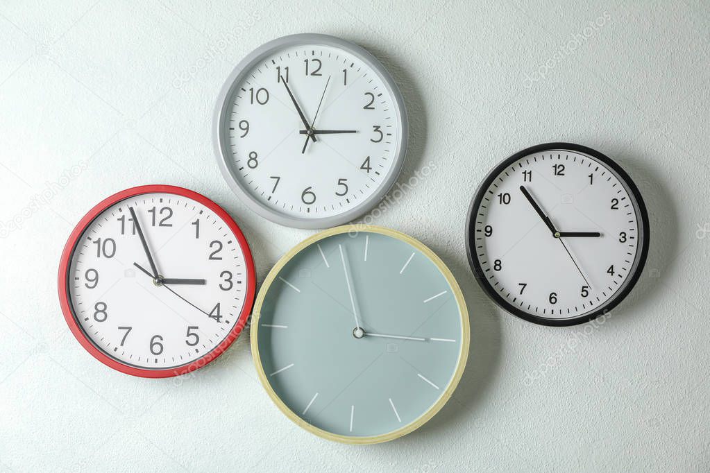 Different beautiful clocks hanging on light wall