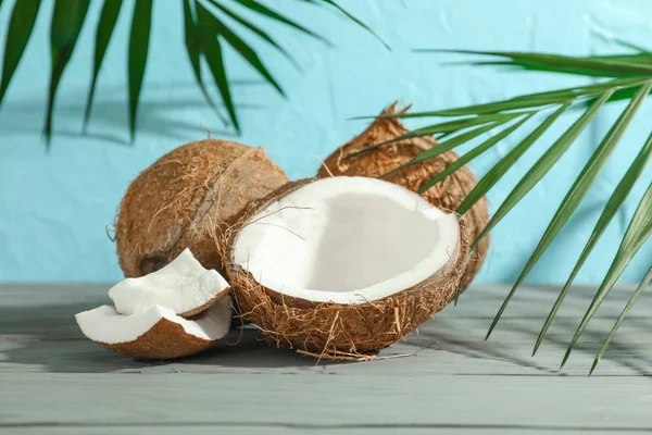 Cocos com ramo de palma na mesa de madeira contra backgrou cor — Fotografia de Stock