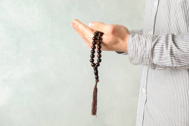 Adam gri arka plana karşı ellerde dua boncuk tutun